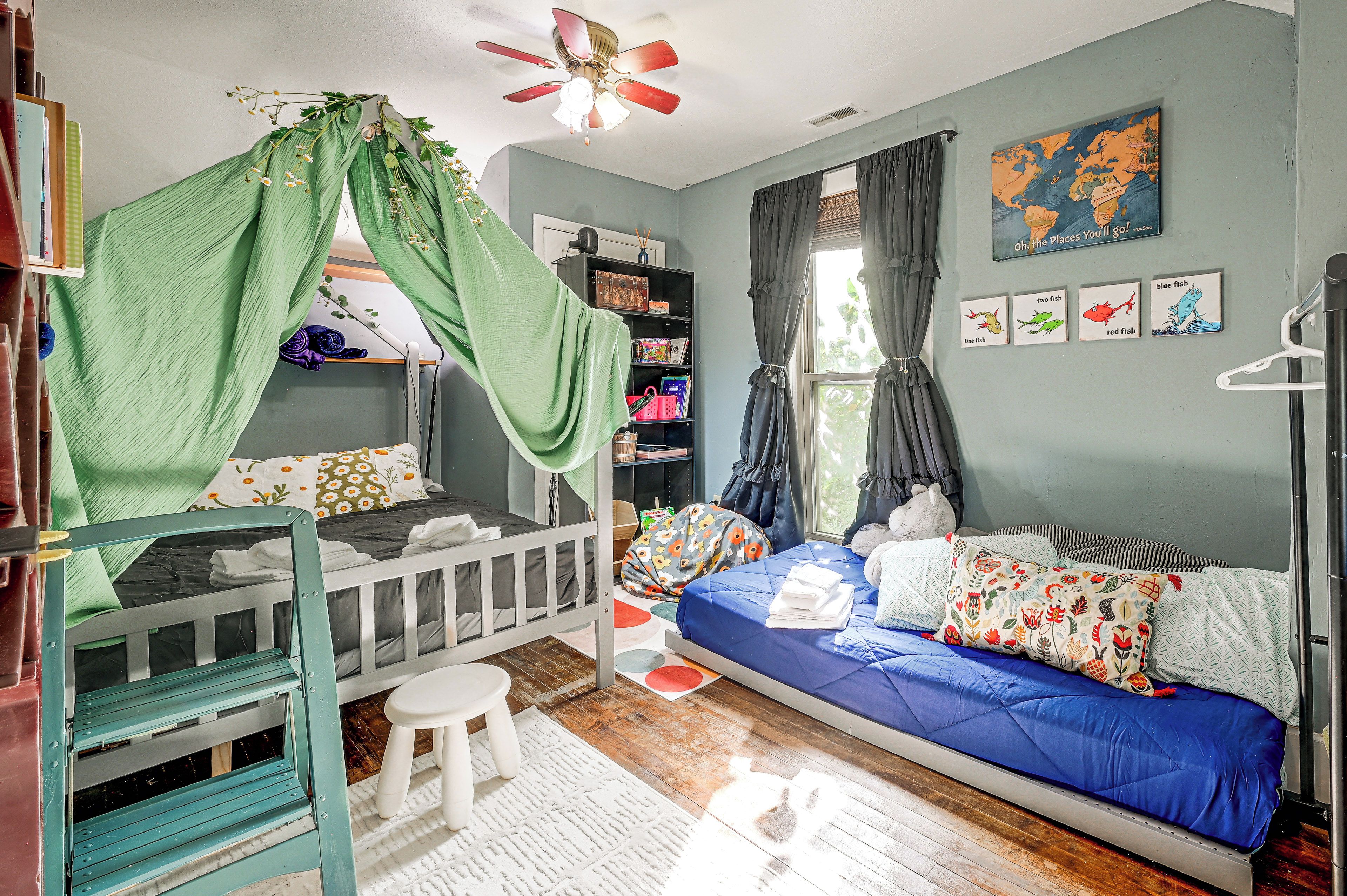 A child's bedroom with a bunk bed, a daybed, a ceiling fan, a bookshelf, and a world map on the wall.