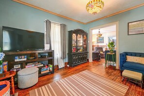 A living room with a television, a cabinet with glass doors, a blue sofa, and a patterned rug. - Historic Des Moines Home: Great for Families! (Des Moines)