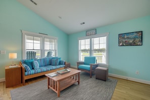 A living room with a sofa, a coffee table, a chair, and a rug. - Sunset & Waterway Views! Holden Beach Getaway (Holden Beach)