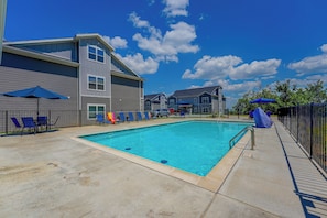A swimming pool with lounge chairs and umbrellas, surrounded by a building with a grey facade. - Condo Near Branson Strip: Close to It All! (Branson)