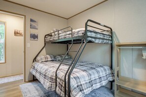 A bunk bed with a checkered bedspread, a small wooden shelf, and a window with a view of trees. - Brand New! Peaceful Wooded Retreat in Holcombe! (Holcombe)