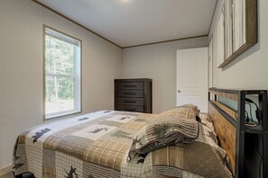 Ein Schlafzimmer mit Bett, Kommode, Tür und Fenster.