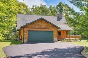 A log cabin with a green garage door, a stone chimney, and a wooden porch. - Ski, Hike & Explore! Spacious Conway Cabin w/ Deck (Albany)