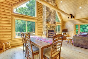 A log cabin interior with a dining area, stone fireplace, and large windows. - Ski, Hike & Explore! Spacious Conway Cabin w/ Deck (Albany)