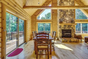 A log cabin interior with a dining area, stone fireplace, and large windows. - Ski, Hike & Explore! Spacious Conway Cabin w/ Deck (Albany)
