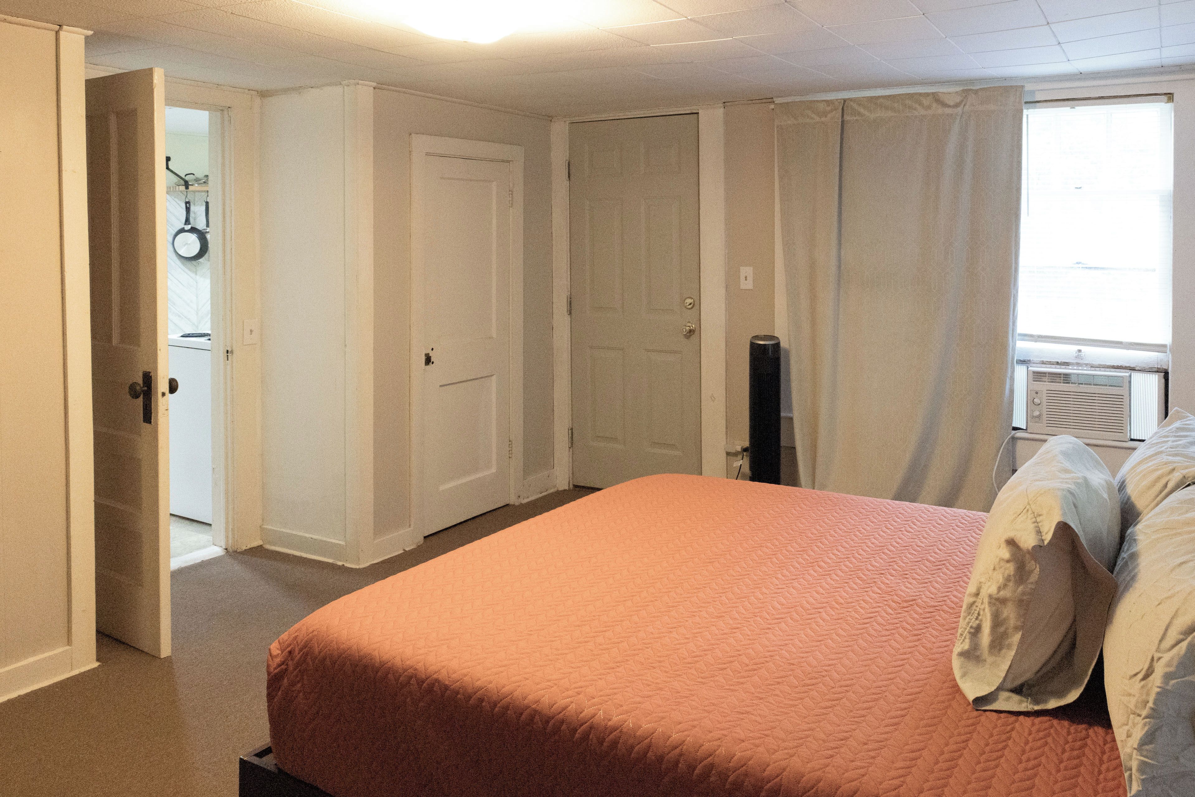 A bedroom with a bed, a door, a window with curtains, and a radiator.