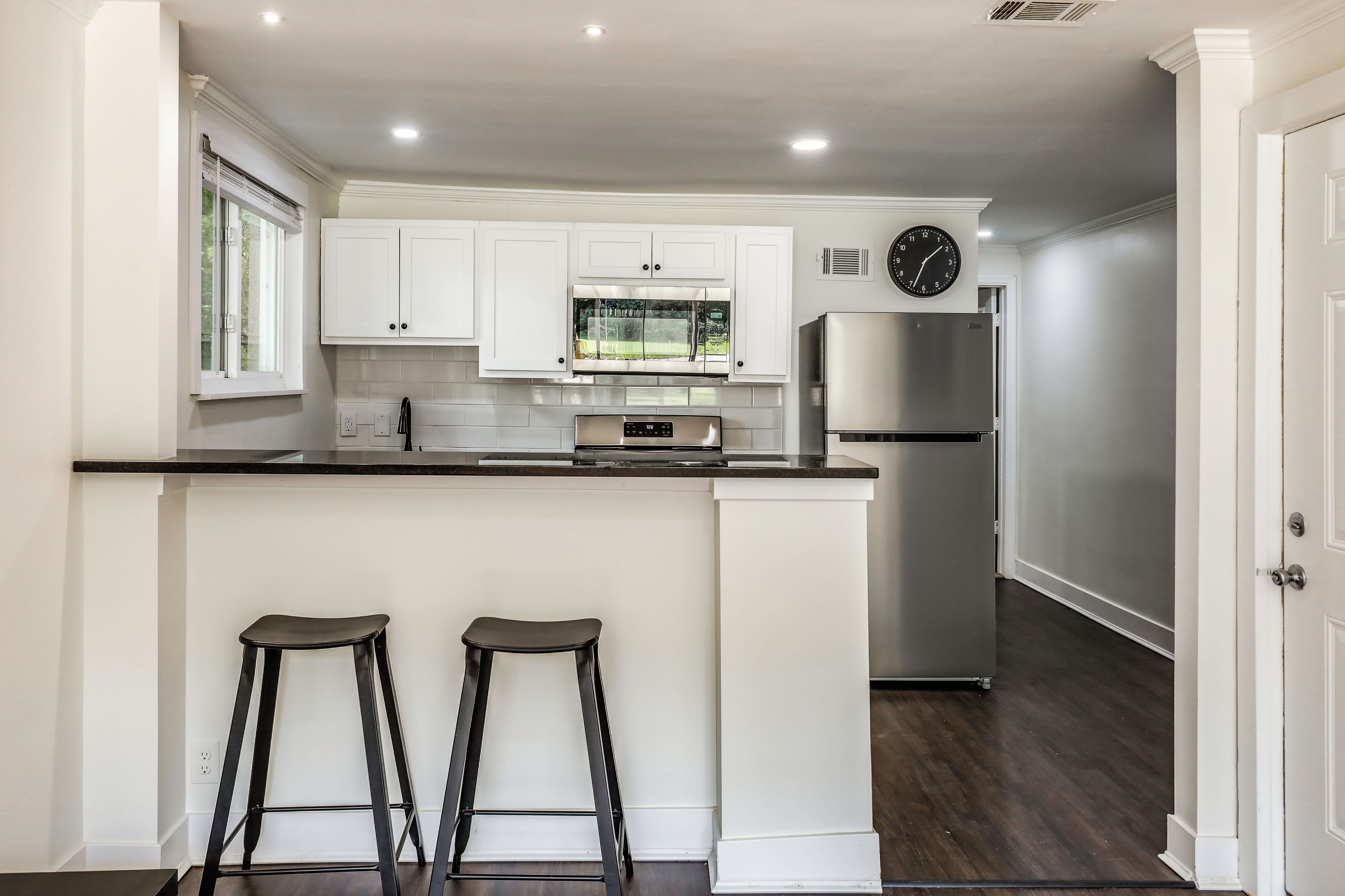 A modern kitchen with white cabinetry, a stainless steel refrigerator, a built-in oven, and a window above the sink.