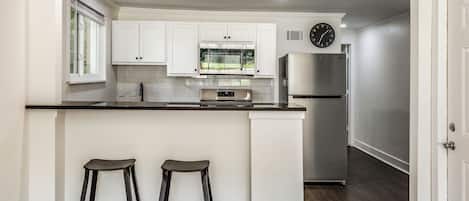 A modern kitchen with white cabinetry, a stainless steel refrigerator, a built-in oven, and a window above the sink.