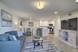 A modern living room with a grey sofa, a glass coffee table, and a kitchen in the background. - Stroll to Shore! 2 Fernandina Beach Condos w/ Pool (Fernandina Beach)