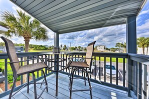 A covered outdoor area with two chairs and a table, overlooking a parking lot and a residential area with palm trees and houses. - Stroll to Shore! 2 Fernandina Beach Condos w/ Pool (Fernandina Beach)