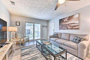 A modern living room with a glass coffee table, a grey sofa, and a large beach-themed painting on the wall. - Stroll to Shore! 2 Fernandina Beach Condos w/ Pool (Fernandina Beach)
