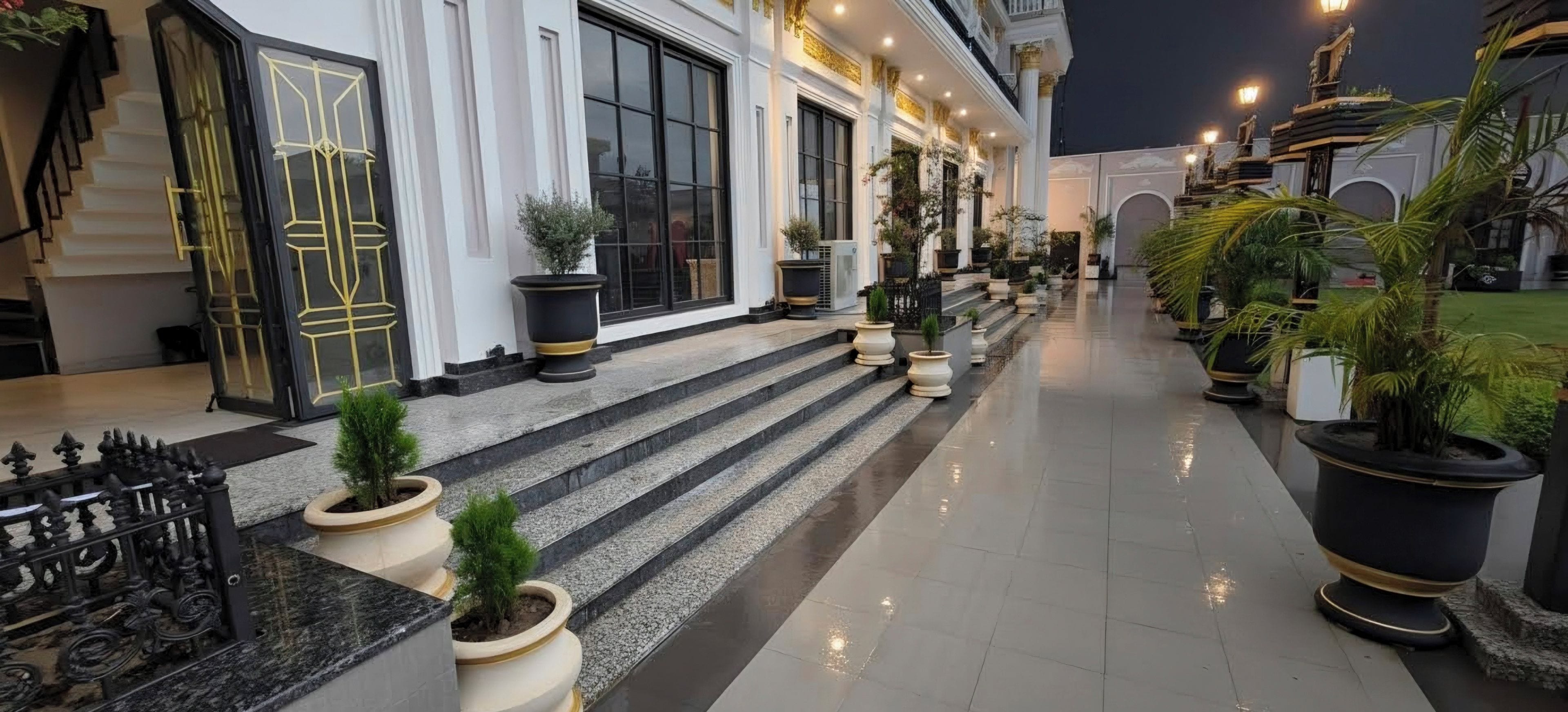 A hotel corridor with steps leading to a door, potted plants, and a railing.