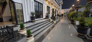 Un pasillo de hotel con escalones que llevan a una puerta, plantas en macetas y una barandilla.