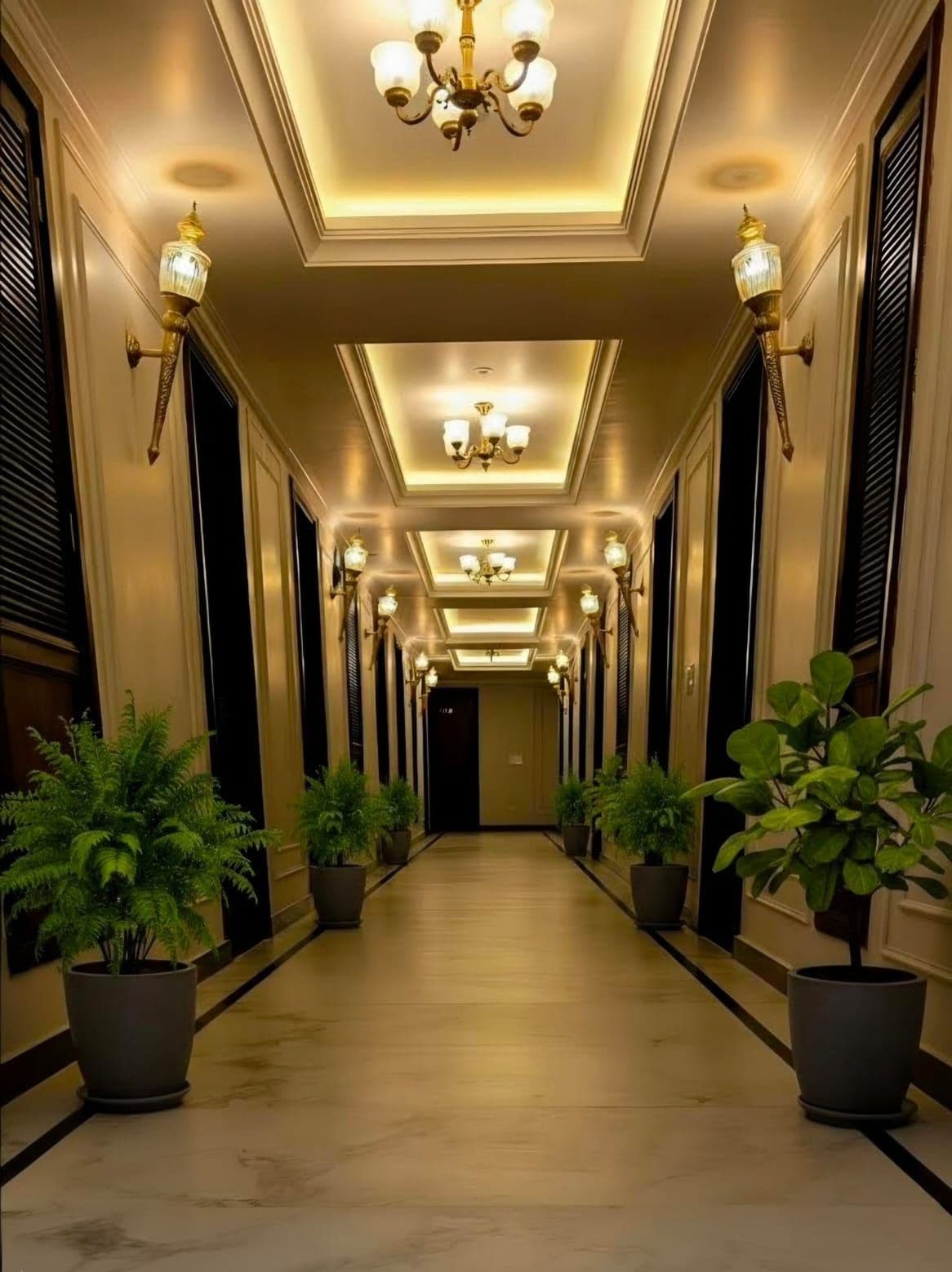 Un pasillo con candelabro, plantas en macetas y una puerta al final.
