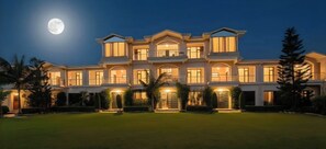 A large, multi-story building with a symmetrical facade, multiple balconies, and a well-maintained lawn in front.