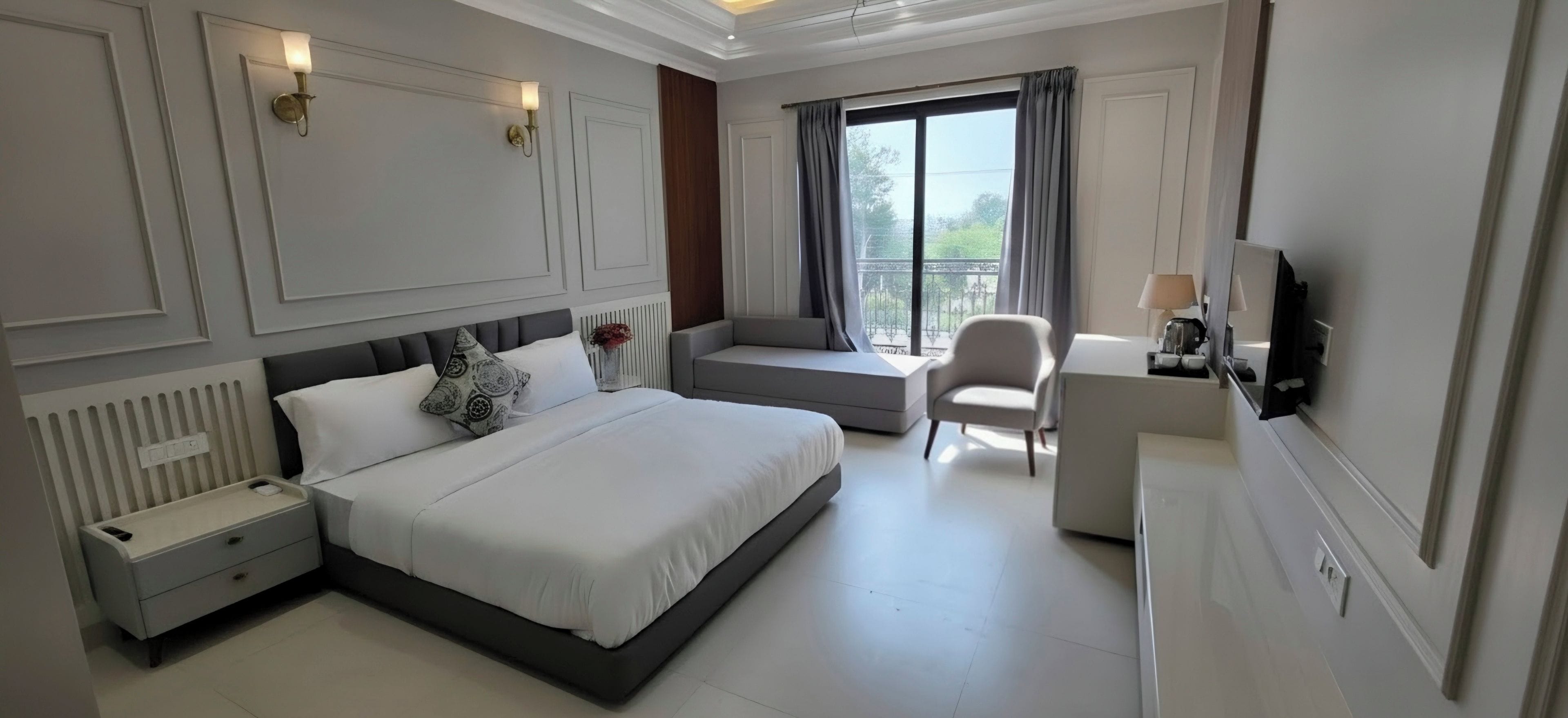 Habitación de hotel con cama, mesita de noche, escritorio, silla, televisor y ventana con cortinas.