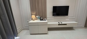 A modern living room with a flat-screen TV mounted on the wall, a white console table with a lamp, and a coffee maker.