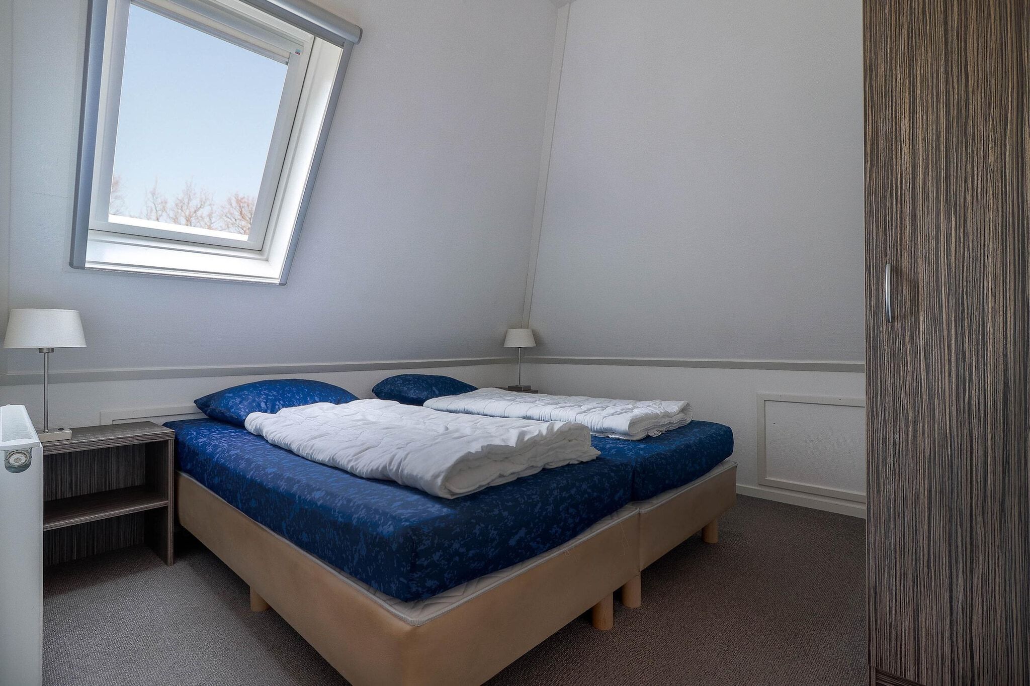 A room with a bed, two bedside tables, a lamp, and a window.