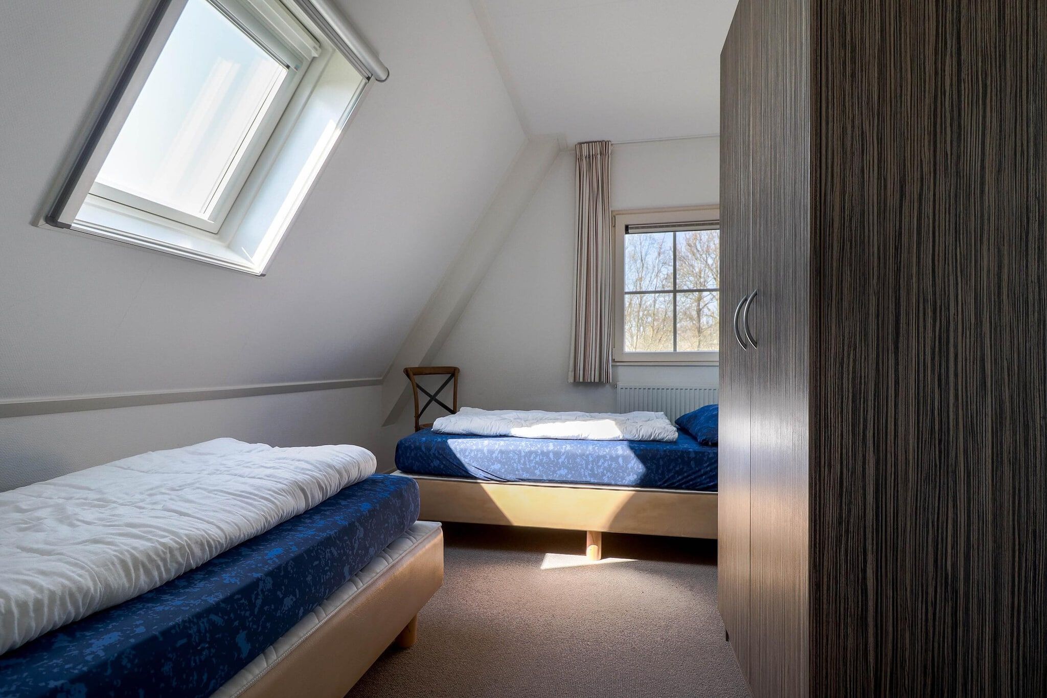 A bedroom with two beds, a window, and a wardrobe.