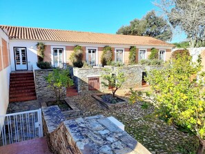 A courtyard with stone steps, a small garden, and a building with a tiled roof. - Naturarte (Odemira)