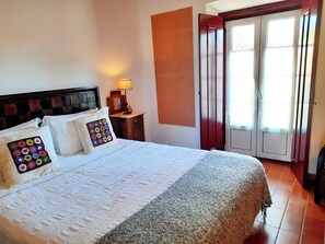 A neatly made bed with a patterned pillow, a bedside lamp, and a view of a sliding door leading to an outdoor area. - Naturarte (Odemira)