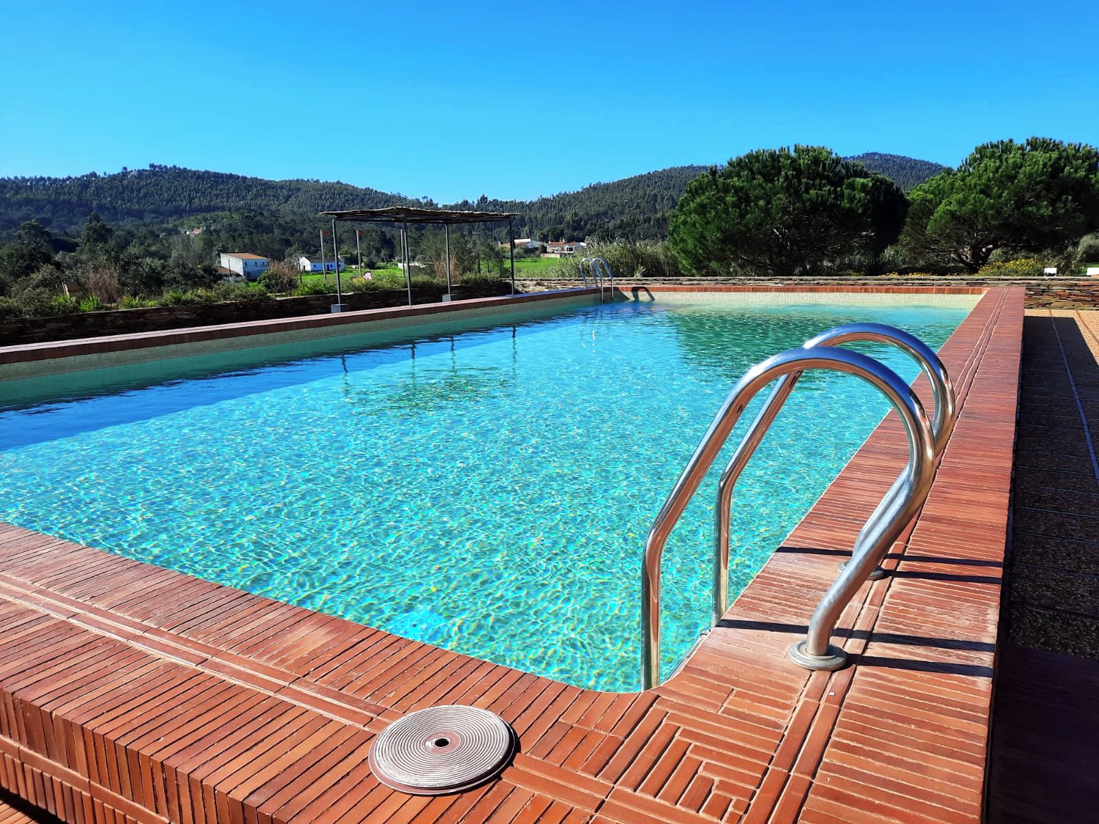 A swimming pool with clear blue water, surrounded by a wooden deck and metal railings.