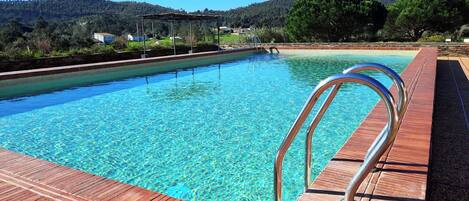 A swimming pool with clear blue water, surrounded by a wooden deck and metal railings.