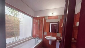 Een badkamer met een bad, een wastafel en een raam met uitzicht op bamboe.