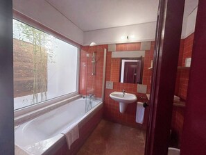 A bathroom with a bathtub, a sink, and a window with a view of bamboo outside. - Naturarte (Odemira)