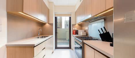 A narrow kitchen with wooden cabinets, a stainless steel sink, and a stove.