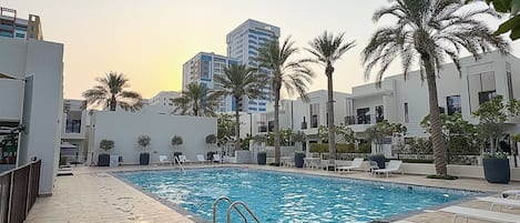 Una piscina con borde de baldosas, rodeada de palmeras y edificios modernos.