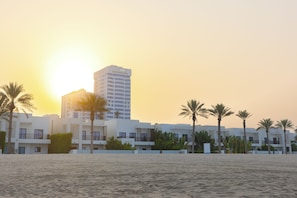 A beachfront hotel with multiple-story buildings, palm trees, and a sandy beach. - Bloomfields 2BR Villa in Eagle Hills  (Al-Fujairah)
