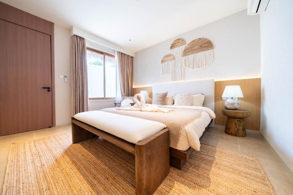 A hotel room with a bed, a bench, a bedside table, a lamp, and a wall-mounted decor piece.