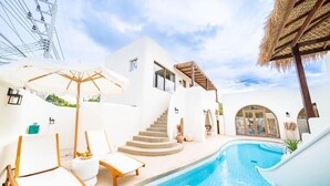 Área de piscina com espreguiçadeiras, escada e estrutura coberta de palha.