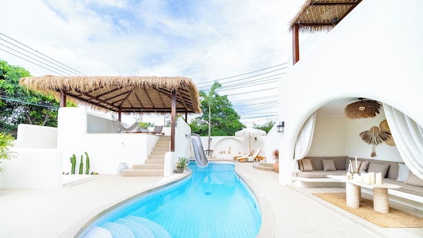 Área de piscina com escorregador, espreguiçadeiras e uma estrutura de telhado de palha.