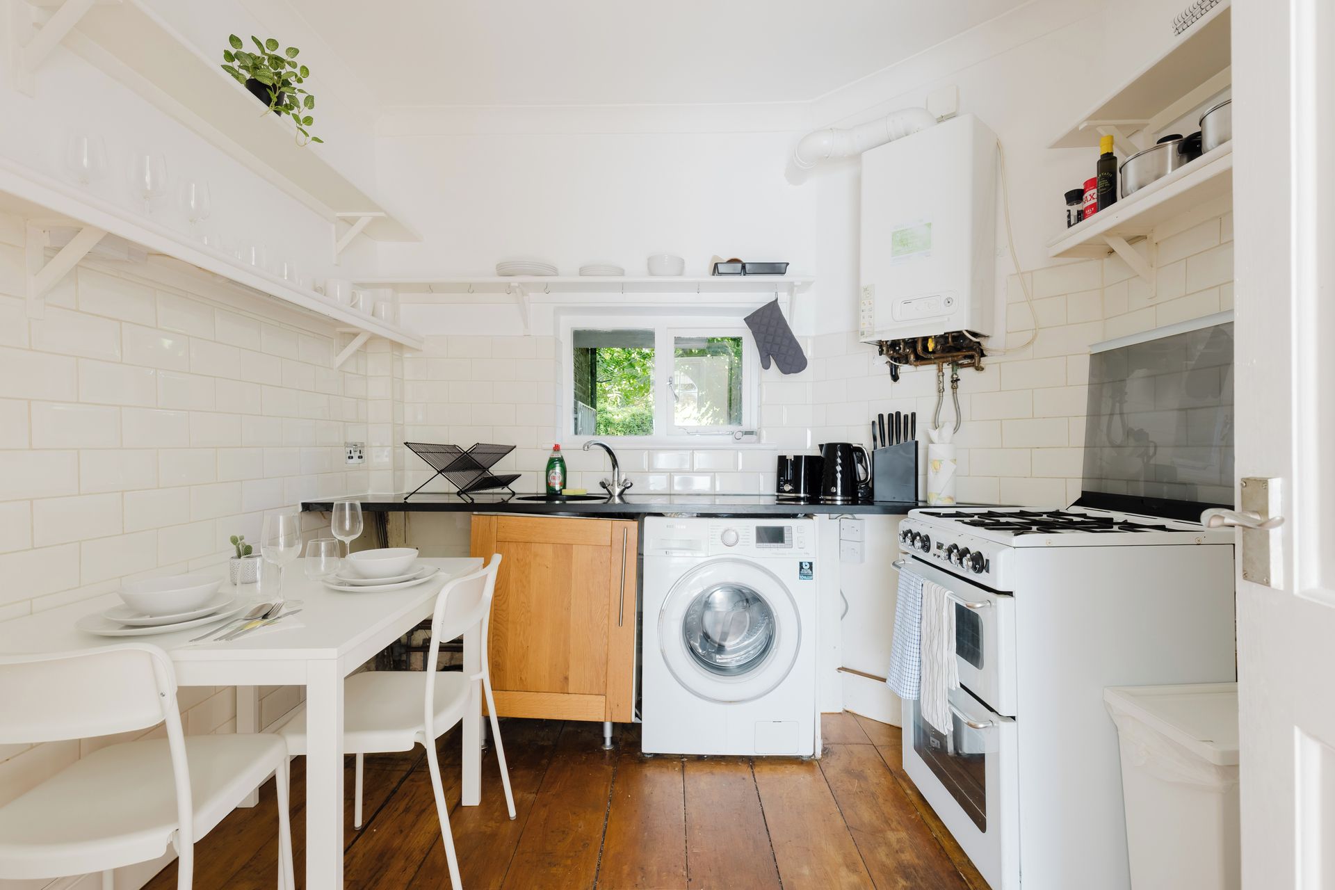Een compacte keuken met een wasmachine, kookplaat en een eethoek met stoelen en een tafel.