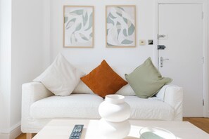 A white sofa with three cushions, a white vase, and a remote control on a white table. - Comfortable 2BDR Flat in Central Whitechapel (Greater London)
