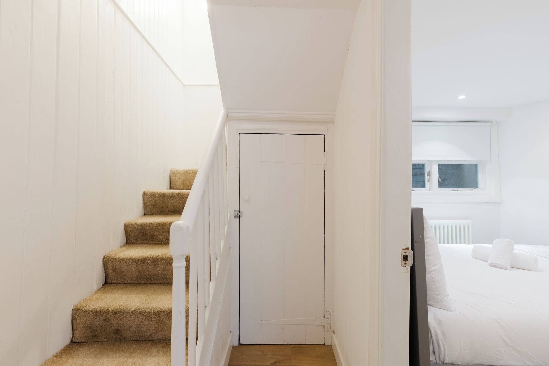 Eine Treppe führt zu einem Schlafzimmer mit einer weißen Tür und einem Fenster über dem Bett.
