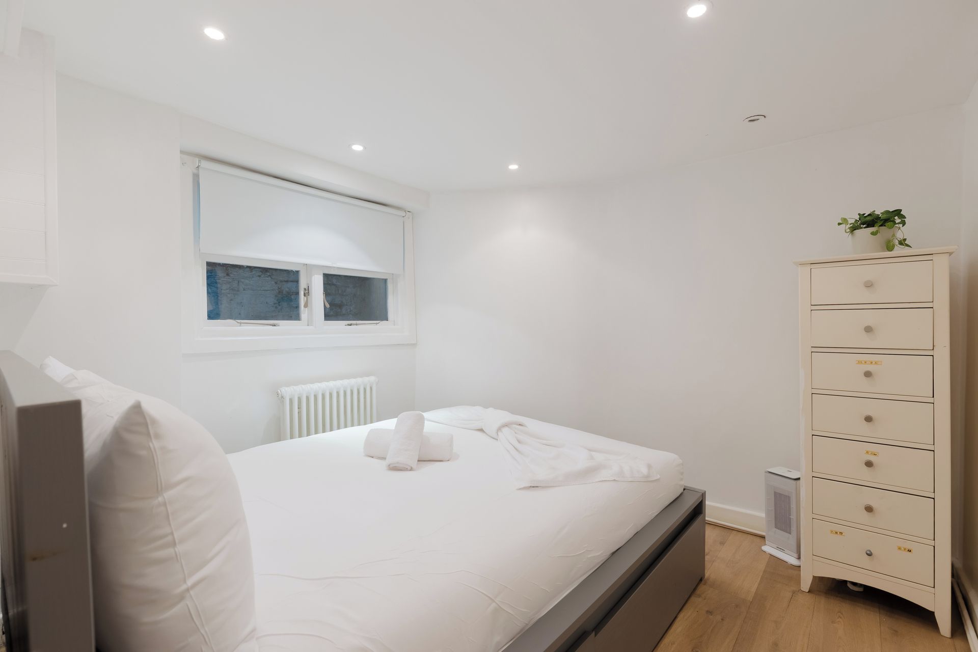 A bedroom with a bed, a dresser, a radiator, and a window with blinds.