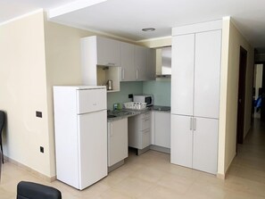 Una cocina compacta con armarios blancos, un refrigerador, un microondas y un lavamanos.