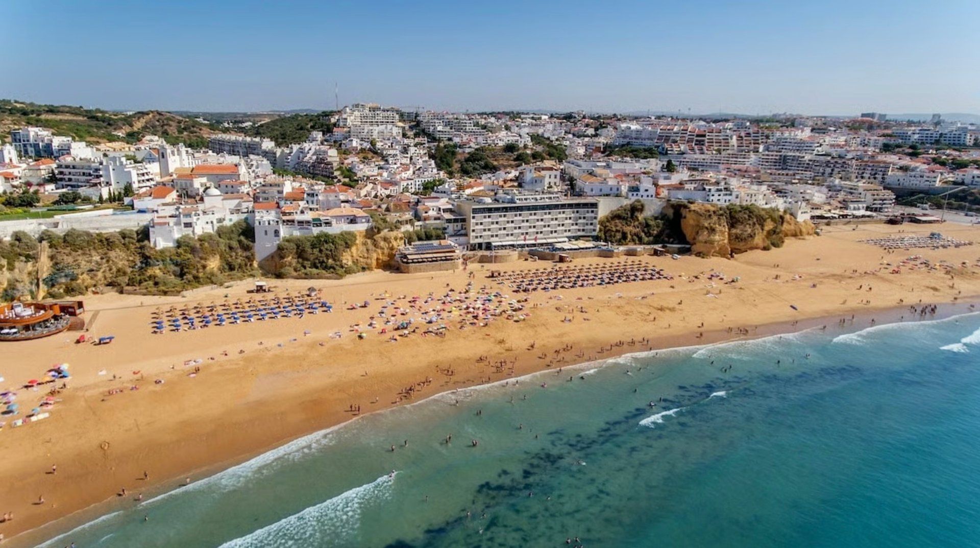 A coastal cityscape with a beach, buildings, and a clear sky.