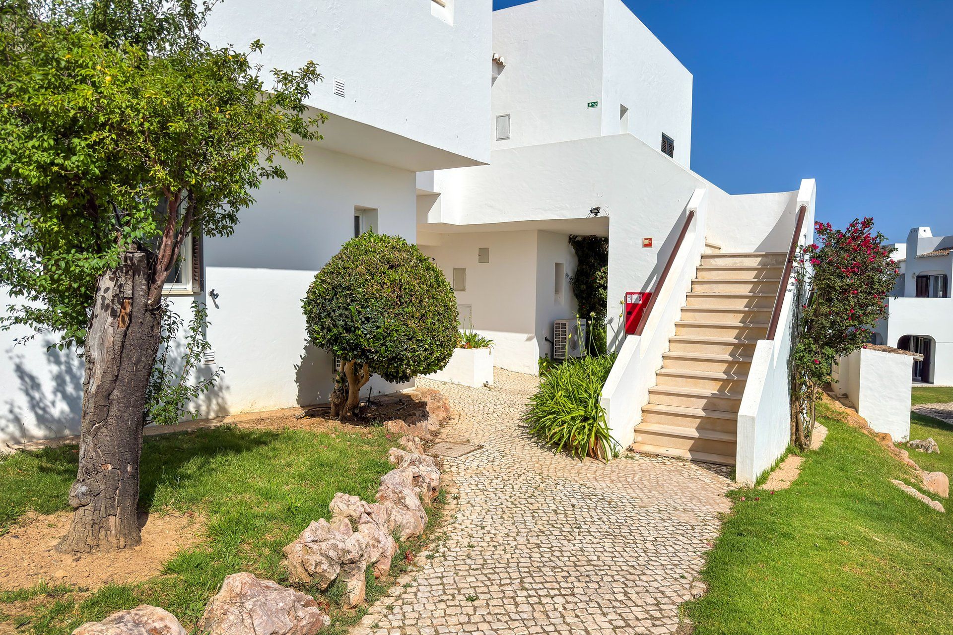 A white building with a cobblestone pathway leading to a staircase.