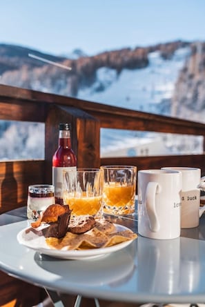 A table with breakfast items, a bottle, and mugs, set against a snowy mountain backdrop. - Maeva Clubhotel Serre Chevalier (Saint-Chaffrey)