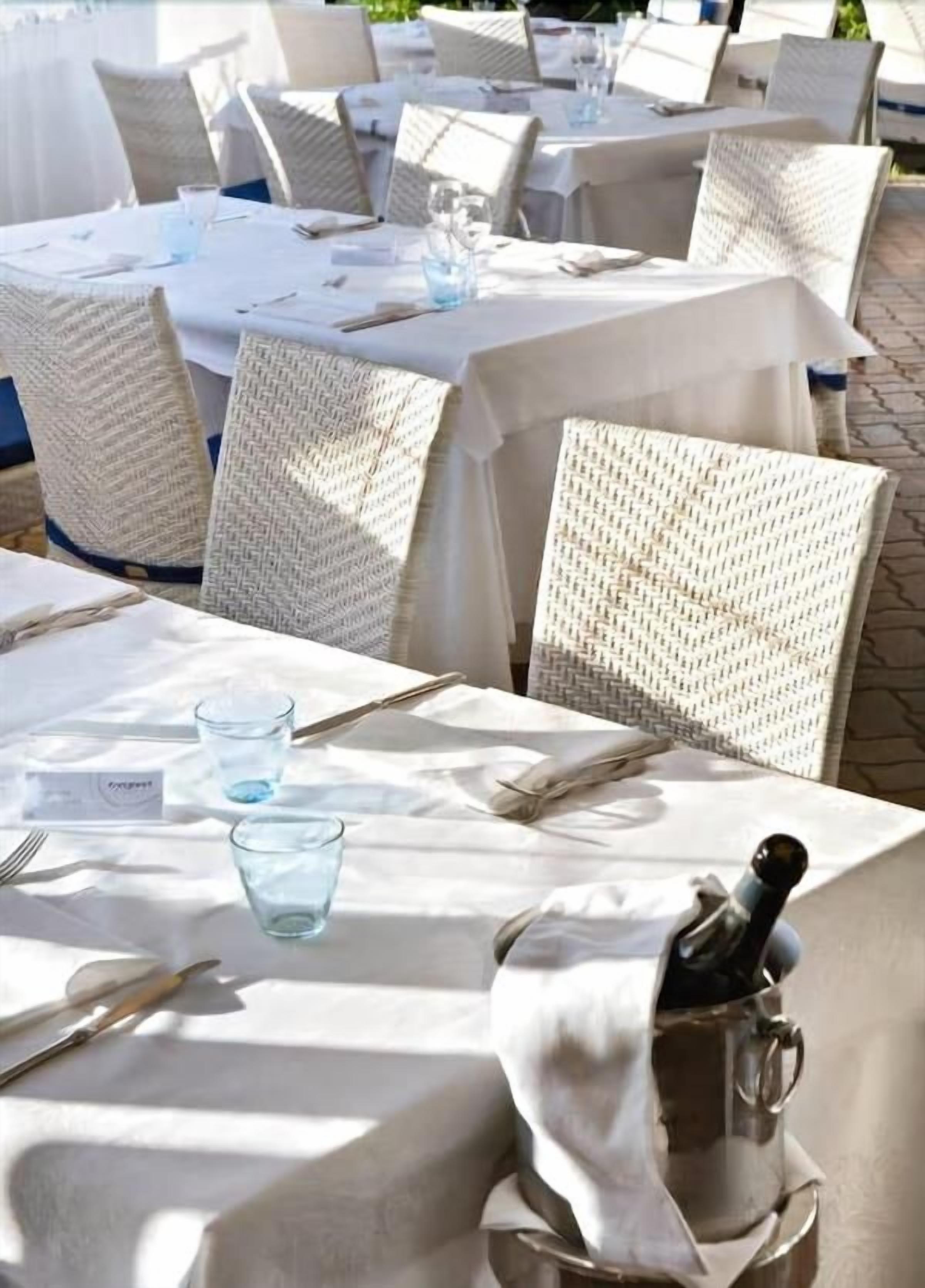 Outdoor dining tables with white tablecloths, wicker chairs, and a bottle of champagne.