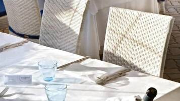 Outdoor dining tables with white tablecloths, wicker chairs, and a bottle of champagne.