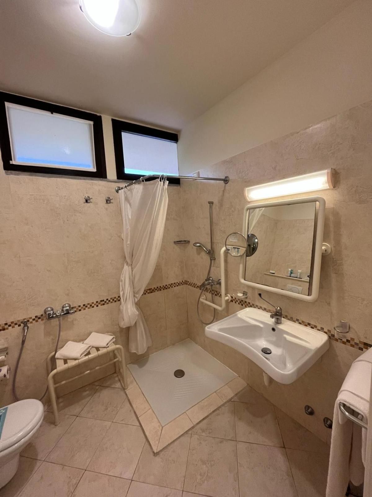A bathroom with a shower, toilet, sink, and a mirror with a light.
