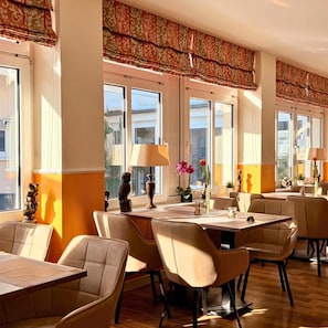 A restaurant with multiple tables and chairs, large windows, and decorative items on the tables. - R and R Strandhotel Baabe (Ostseebad Baabe)