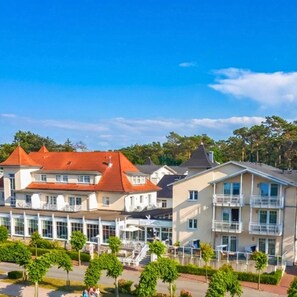 A residential area with multi-story buildings, a clear sky, and a well-maintained green space with trees. - R and R Strandhotel Baabe (Ostseebad Baabe)