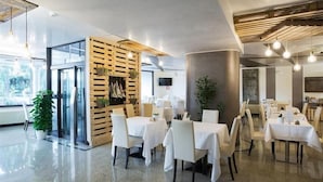 A modern restaurant interior with tables and chairs, a wooden partition, and a large window. - Mefuta Hotel (Gardone Riviera)