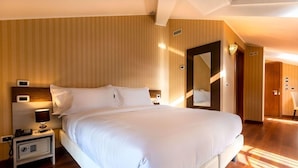 A hotel room with a large bed, a bedside table with a lamp, a safe, and a mirror. - Mefuta Hotel (Gardone Riviera)